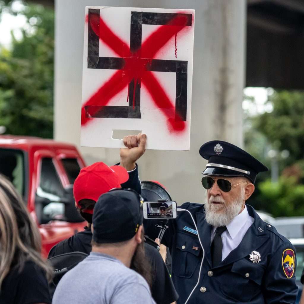 A man is holding a swastika sign with a red cross through.